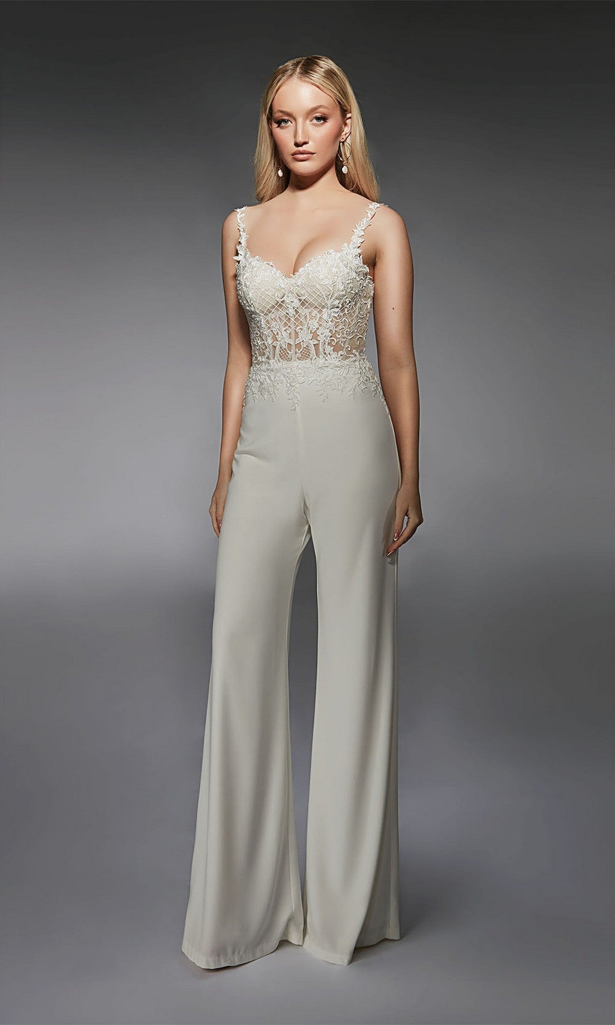 A woman models the Alyce 70074 Long Formal Jumpsuit in diamond white, featuring a sheer lace bodice with floral embroidery and wide-leg pants, set against a gray background.